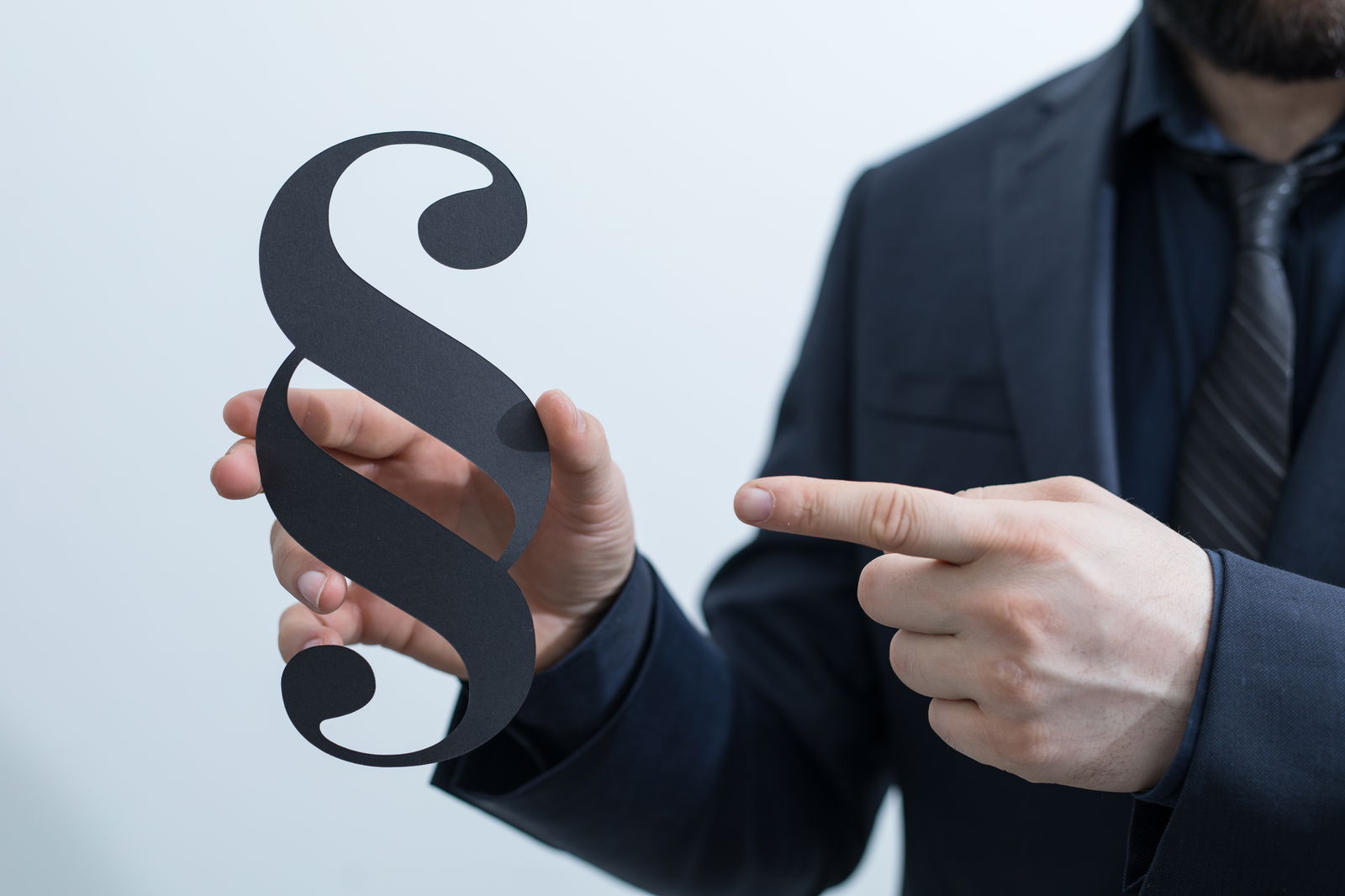 Eine Person hält mit der rechten Hand ein Paragrafen-Zeichen und zeigt mit der linken Hand darauf