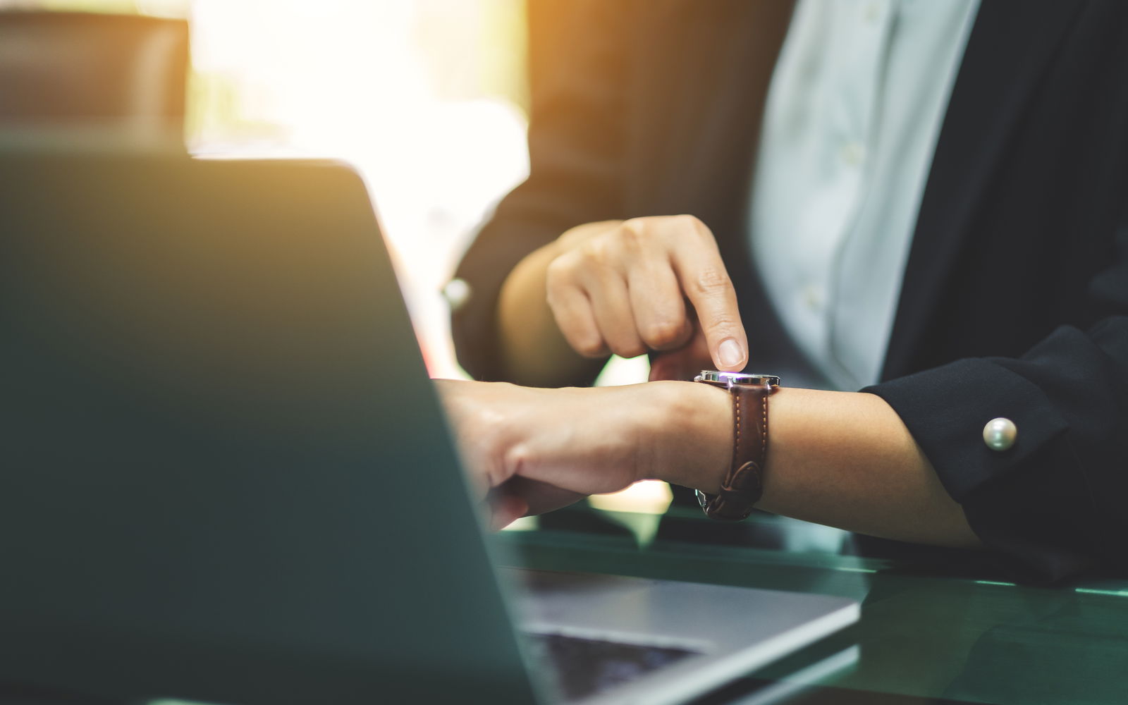 Eine Person zeigt auf ihre Armbanduhr , während sie vor ihrem Laptop sitzt